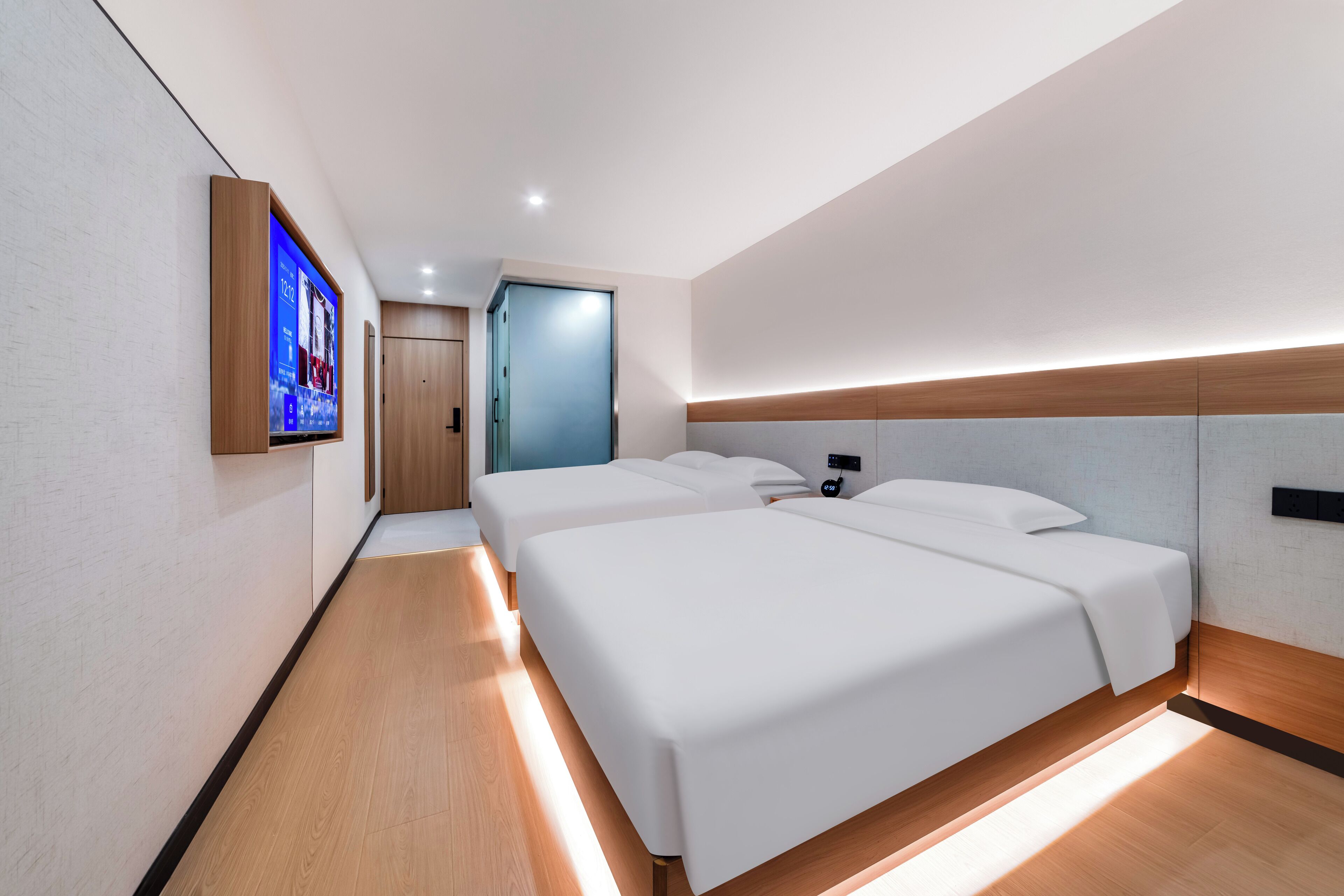A modern hotel room with two beds, a flat-screen TV mounted on the wall, and a wooden floor.