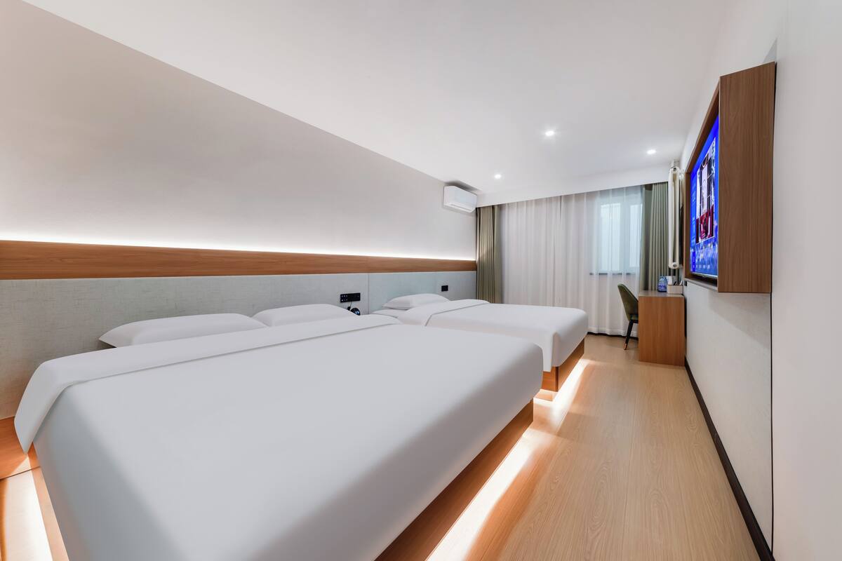 Een hotelkamer met twee bedden, een bureau, een stoel, een televisie en een raam met gordijnen.