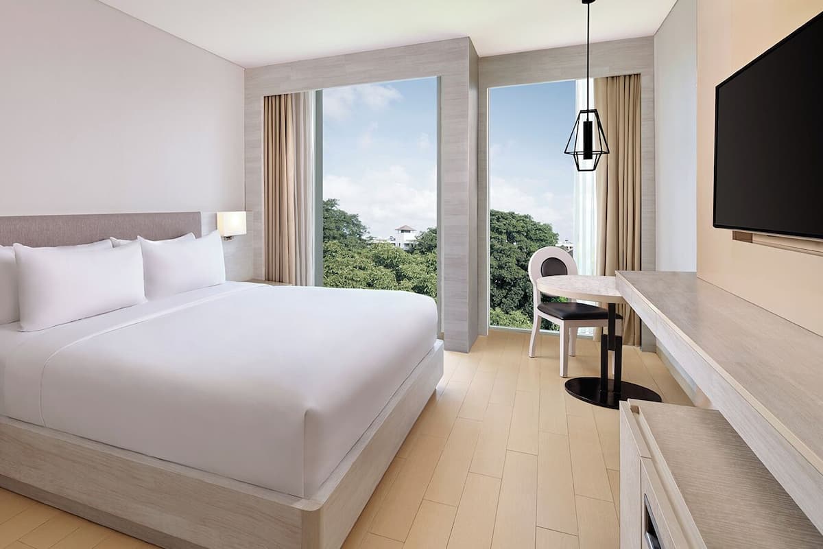Une chambre d’hôtel moderne dotée d’un grand lit, d’un bureau avec une chaise, d’une télévision et offrant une vue sur la verdure.