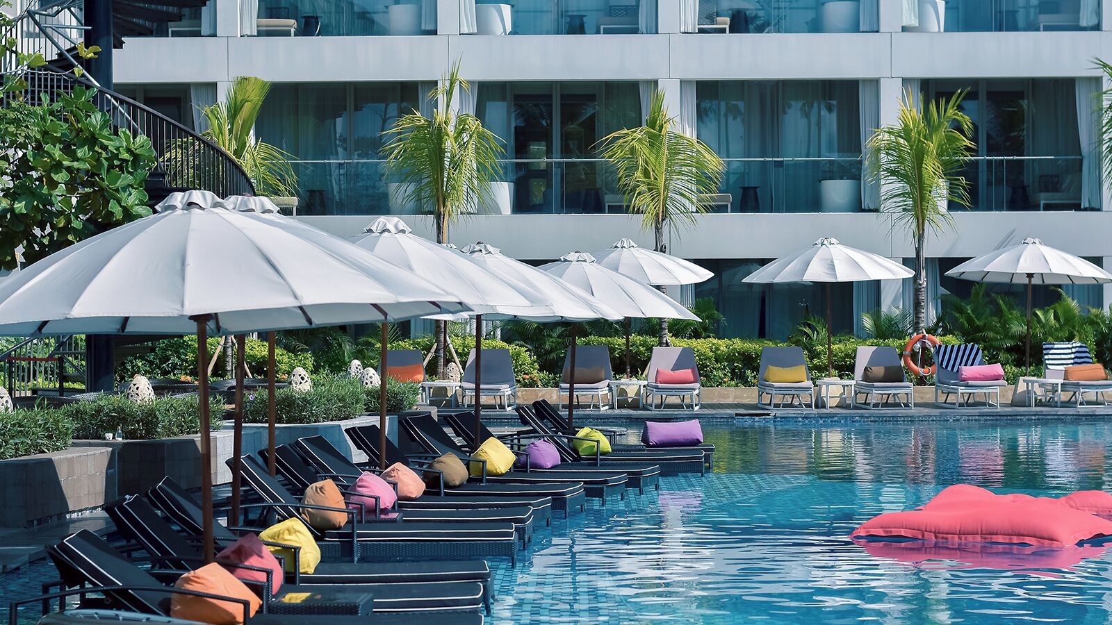A poolside area with lounge chairs and umbrellas, a swimming pool, and a modern building in the background.