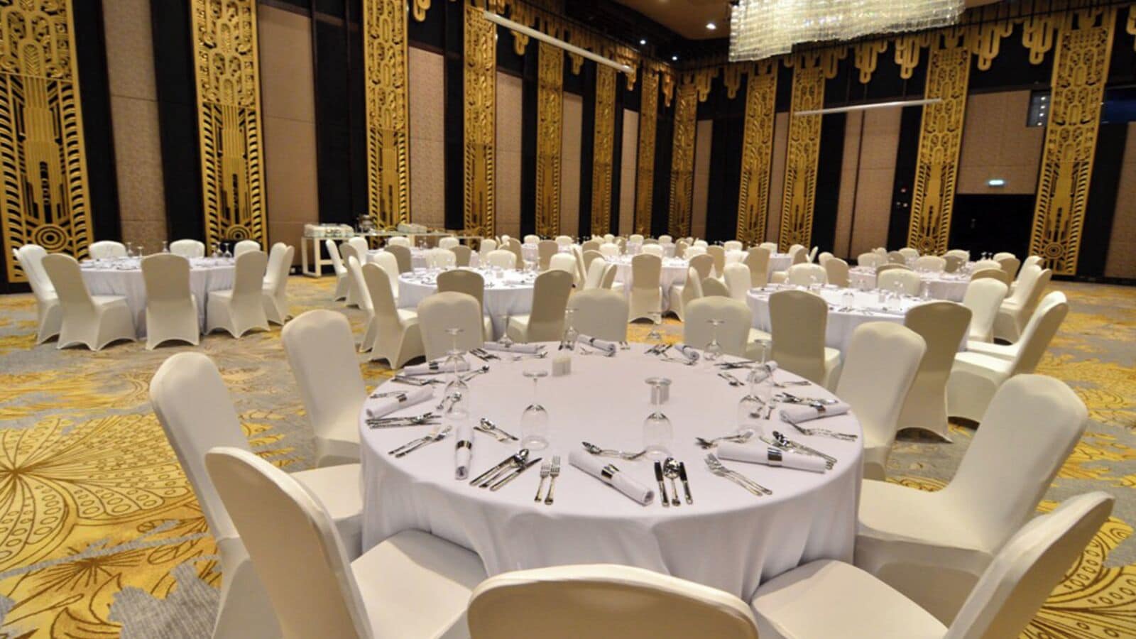 A banquet hall with round tables set for a formal event, surrounded by white chairs.