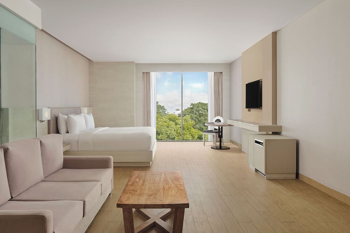 Une chambre d’hôtel moderne équipée d’un canapé, d’un lit, d’une table à manger, d’une télévision et offrant une vue sur la verdure environnante.