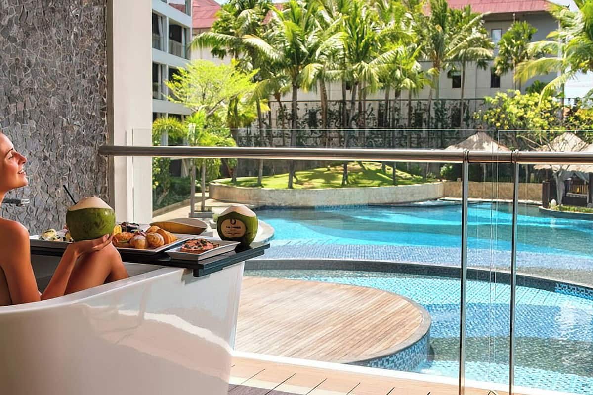 Une personne dans une baignoire, avec vue sur une piscine et des palmiers.