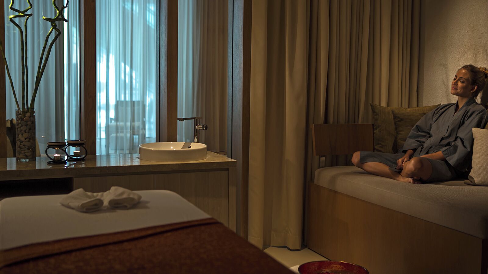 Quarto de hotel com cama, mesa de cabeceira, pia e janela com cortinas.