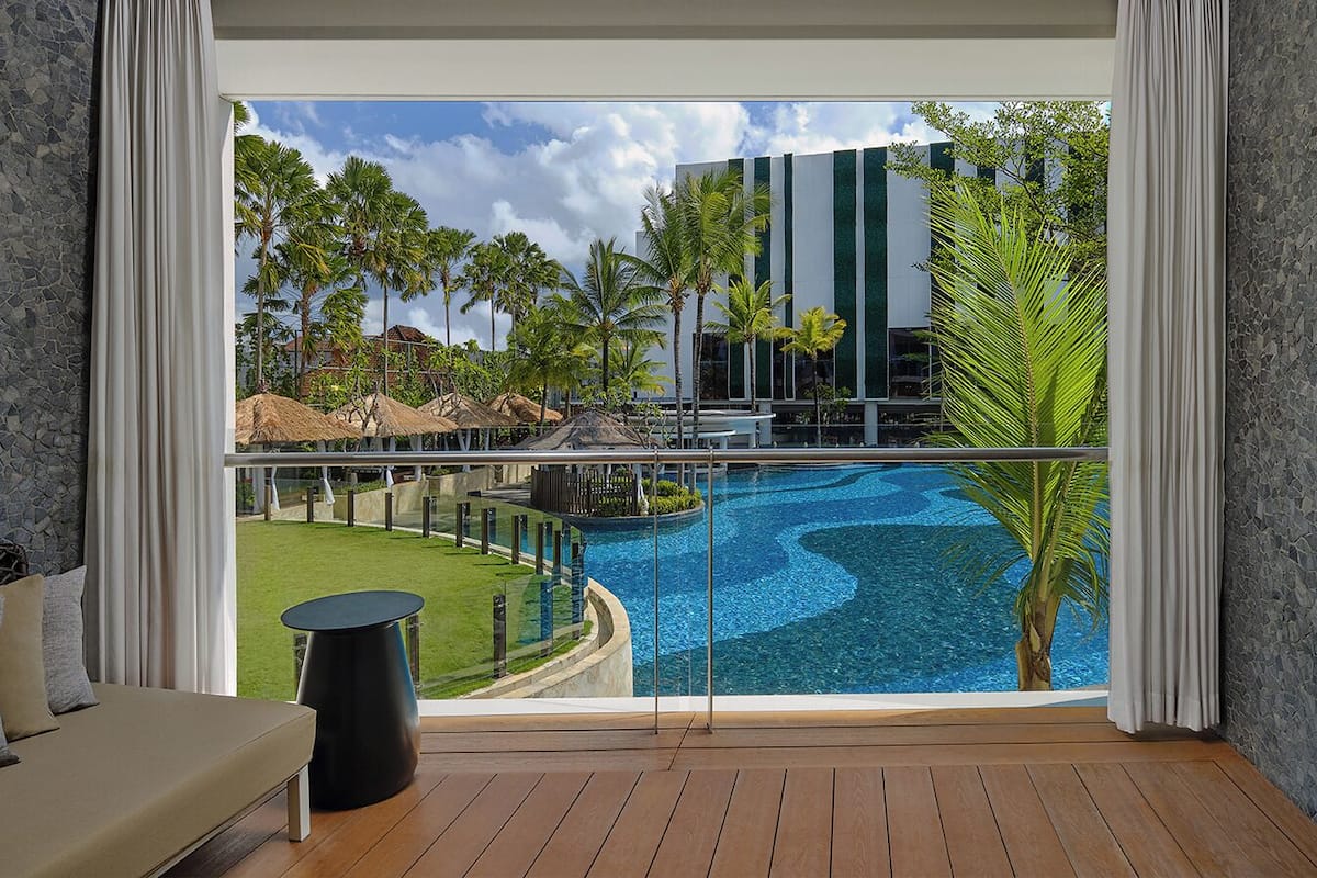 Un balcon donnant sur une piscine, une pelouse et un bâtiment orné de bandes vertes verticales.