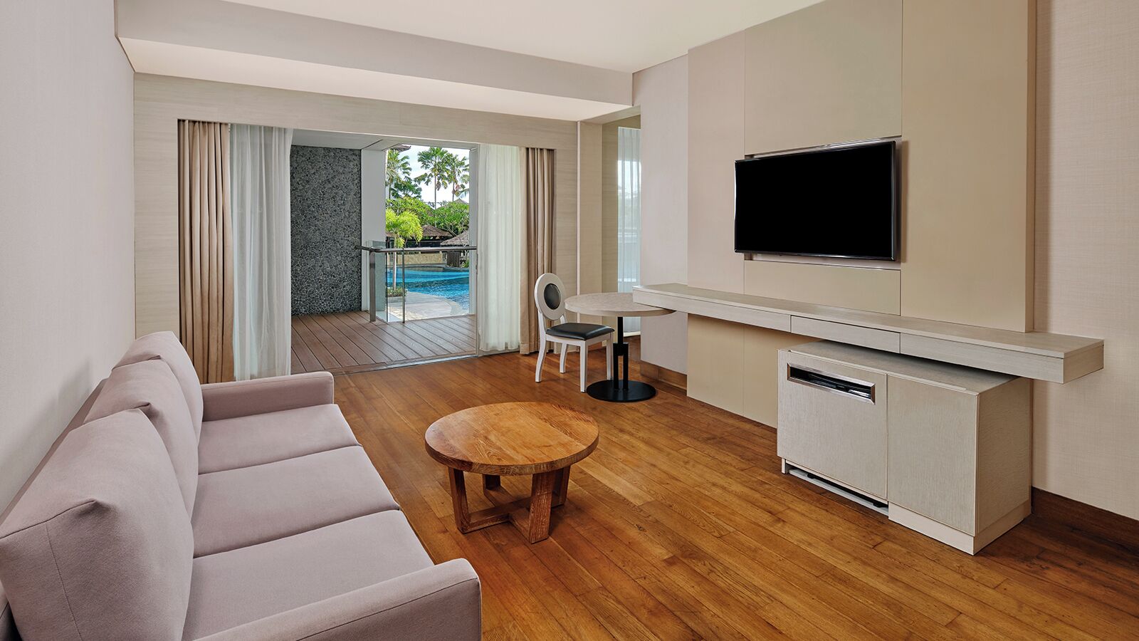 A modern living room with a sofa, a round wooden table, and a TV mounted on the wall.