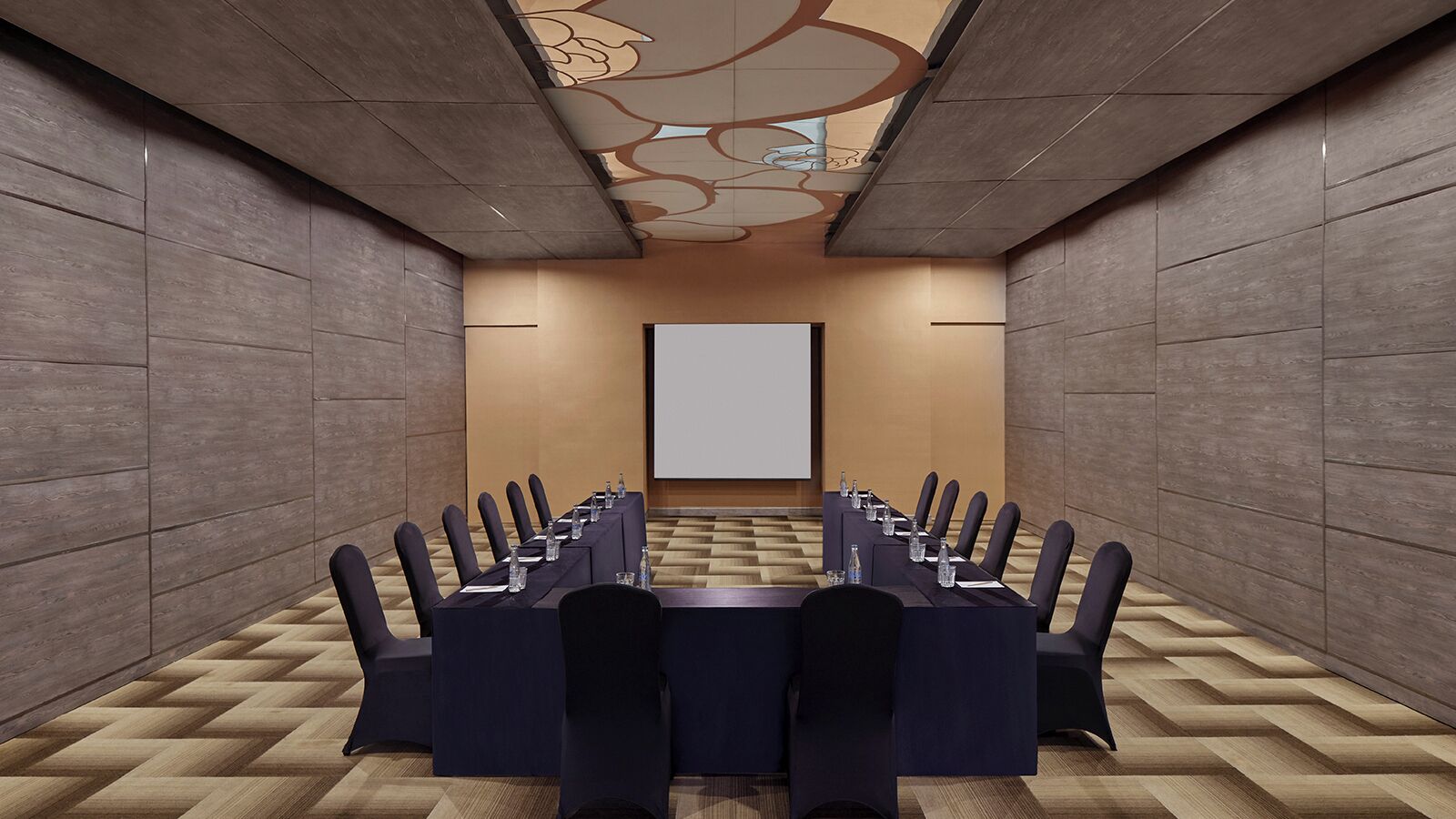 A conference room with a long table, chairs, and a projector screen.