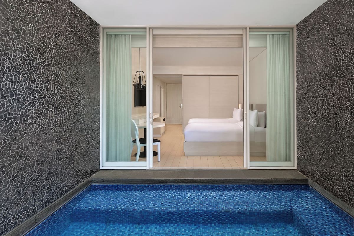 Une chambre d’hôtel moderne dotée d’une porte vitrée donnant sur un balcon, d’un petit coin salon et d’un grand lit.