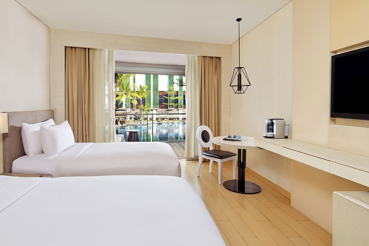 Une chambre d’hôtel avec deux lits, un bureau, une chaise, une télévision et une vue sur une piscine et un espace verdoyant.