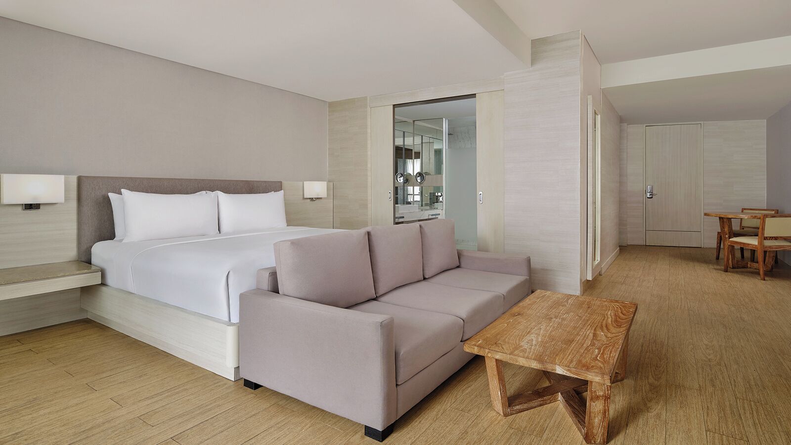 Ett modernt hotellrum med en säng, soffa, ett träbord och en liten matplats.