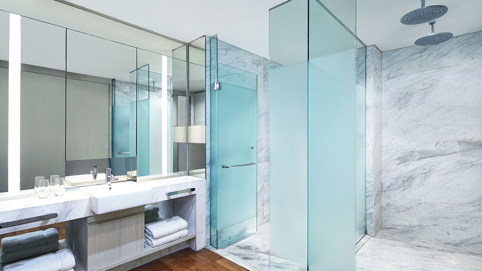 A modern bathroom with a glass-enclosed shower, marble walls, and a large mirror above the sink.