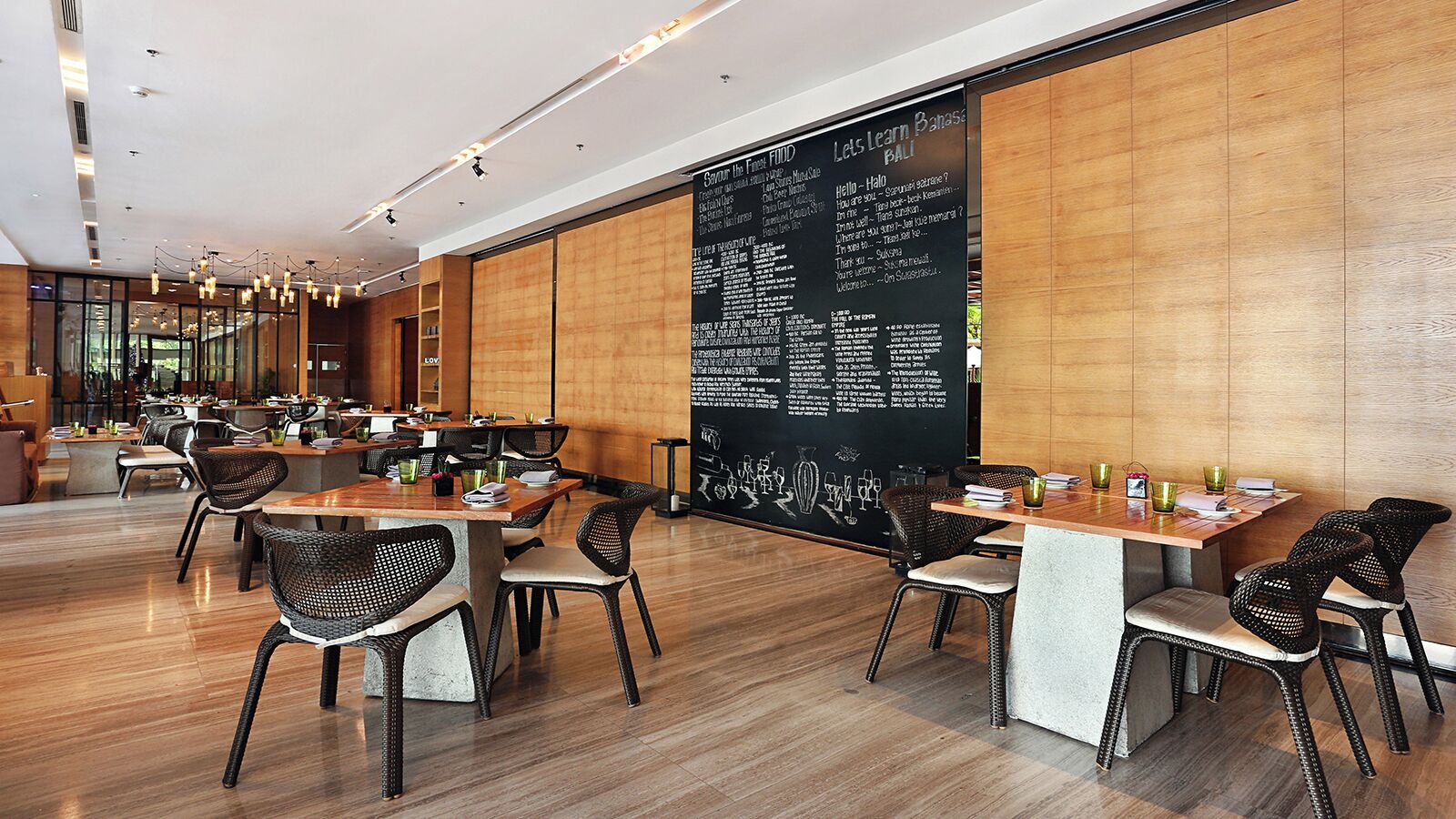 Un ristorante moderno con pavimento in legno, sedie in vimini bianco e nero e un'ampia lavagna con il menu.