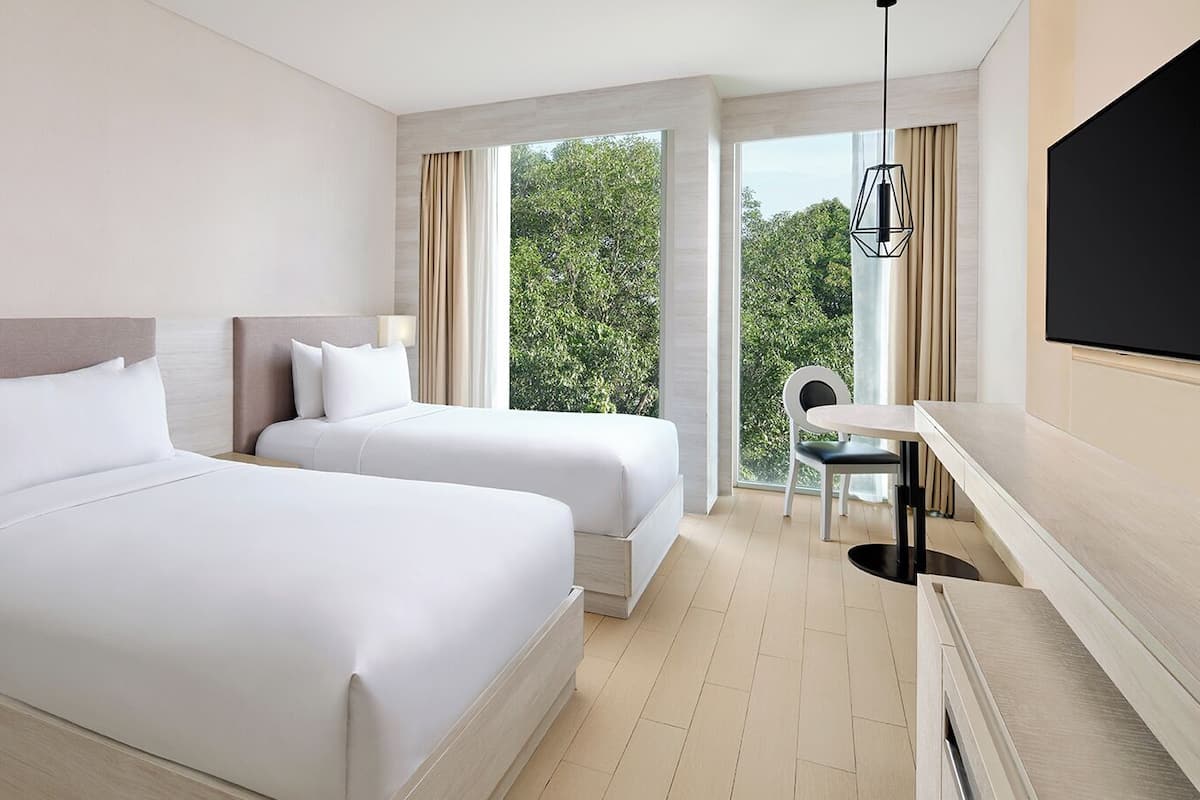 Une chambre d’hôtel avec deux lits, une télévision, un bureau et une fenêtre donnant sur des arbres.