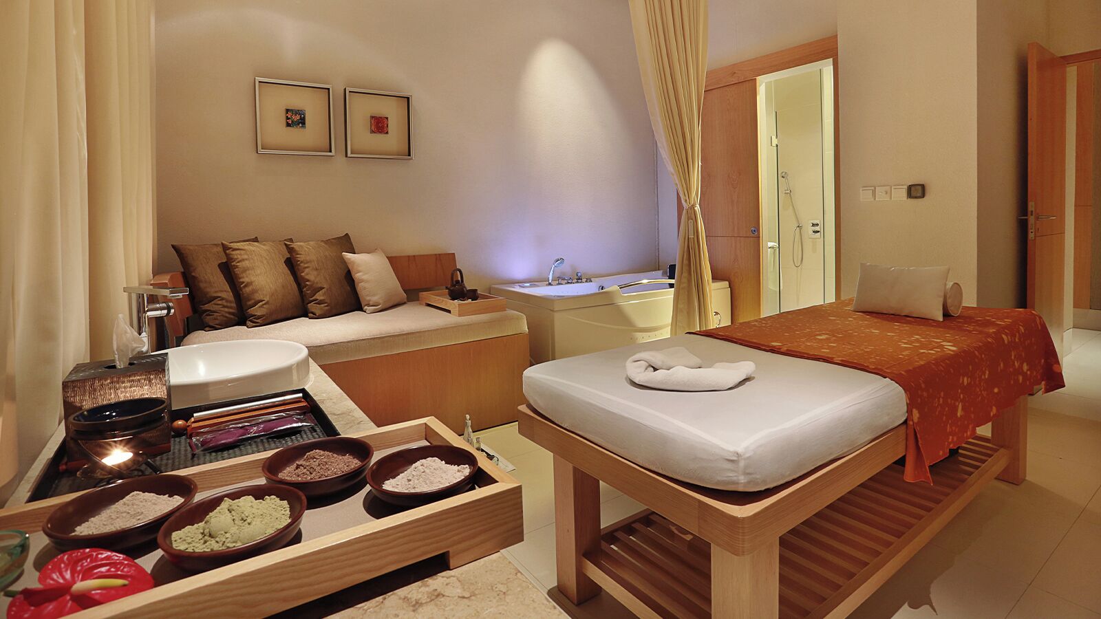 Quarto de hotel com cama, sofá, pequena mesa com tigelas, pia e área de chuveiro.