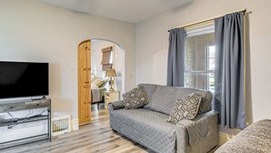 Un salon avec un canapé gris, un téléviseur à écran plat et une porte en bois donnant sur une autre pièce.