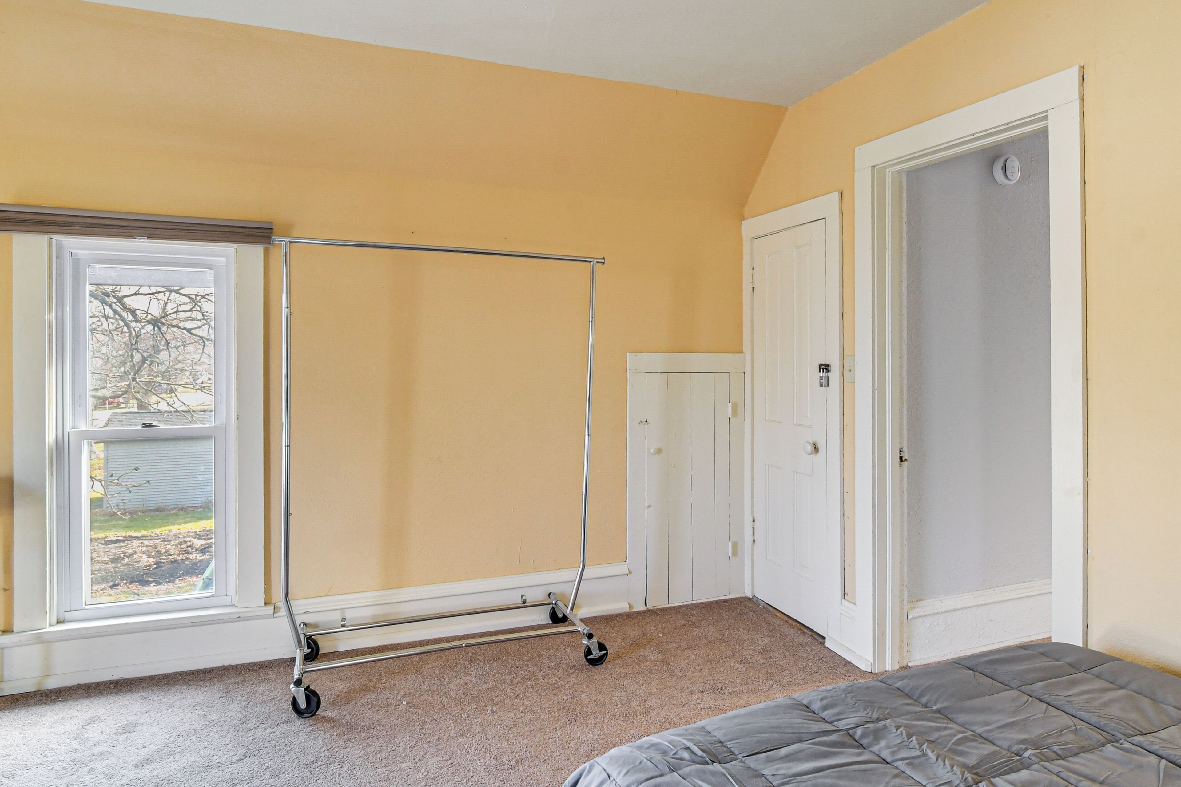 Una habitación con cama, ventana de metal y puerta.