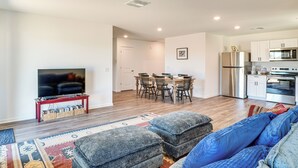 Un salon moderne comprenant un téléviseur, des poufs, un canapé et un coin repas avec des chaises et une table.