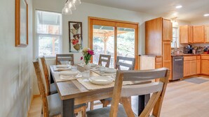 Un coin repas avec une table en bois dressée pour quatre personnes, entourée de chaises, et donnant sur l’extérieur grâce à une porte vitrée.