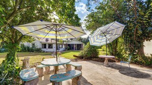 A patio with stone tables and chairs, two striped umbrellas, and a house in the background.