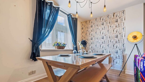 A dining area with a wooden table, benches, a potted plant, and a wall with framed pictures. - Pontypool Haven Retreat - 3Bedroom Flat (Torfaen Principal Area)