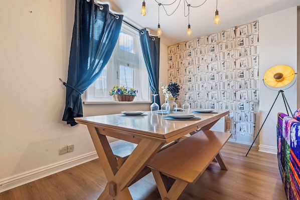 A dining area with a wooden table, benches, a potted plant, and a wall with framed pictures.