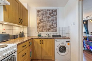 A compact kitchen with wooden cabinets, a built-in washing machine, and a tiled backsplash.