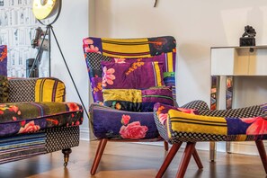A chair with a patchwork design, a lamp, and a bookshelf.