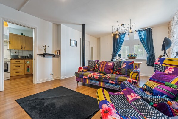 A living room with a colorful sofa, a black rug, and a kitchen visible in the background.