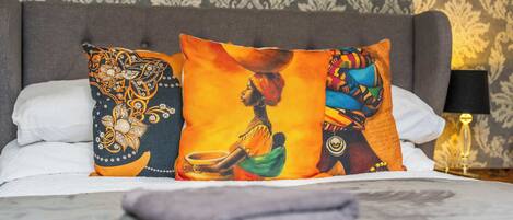 Una cama con almohadones decorativos, una lámpara y un papel tapiz estampado.