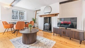 Un salon moderne avec une cheminée, un coin repas avec des chaises orange, une table basse ronde et un téléviseur affichant le logo de Netflix.