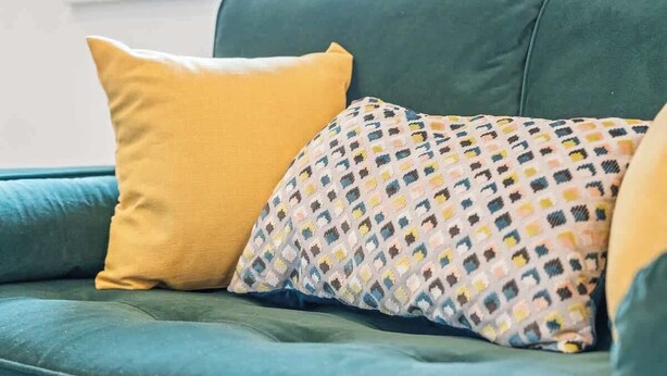 Un canapé vert avec deux coussins, un jaune et l’autre à motifs multicolores.