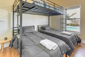 Une chambre avec un lit superposé, deux lits, une petite table et une fenêtre donnant sur une piscine.