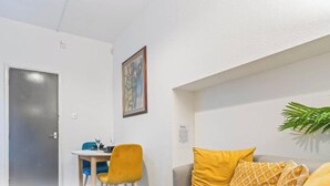 Una habitación con televisión mostrando el logotipo de Netflix, una mesa de comedor con sillas, un sofá con cojines amarillos y un cuadro en la pared.