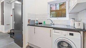 Cocina compacta con lavadora, lavamanos y ventana con vistas al exterior.