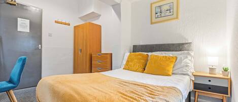 A bedroom with a bed, a nightstand, a wooden wardrobe, a blue chair, and a door with a sign.