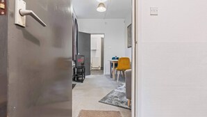 Un pasillo con una puerta, un radiador, una mesa con sillas y una alfombra.