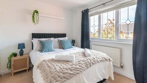 Une chambre à coucher avec un lit, des tables de chevet, une plante suspendue, une fenêtre avec des rideaux et un radiateur.