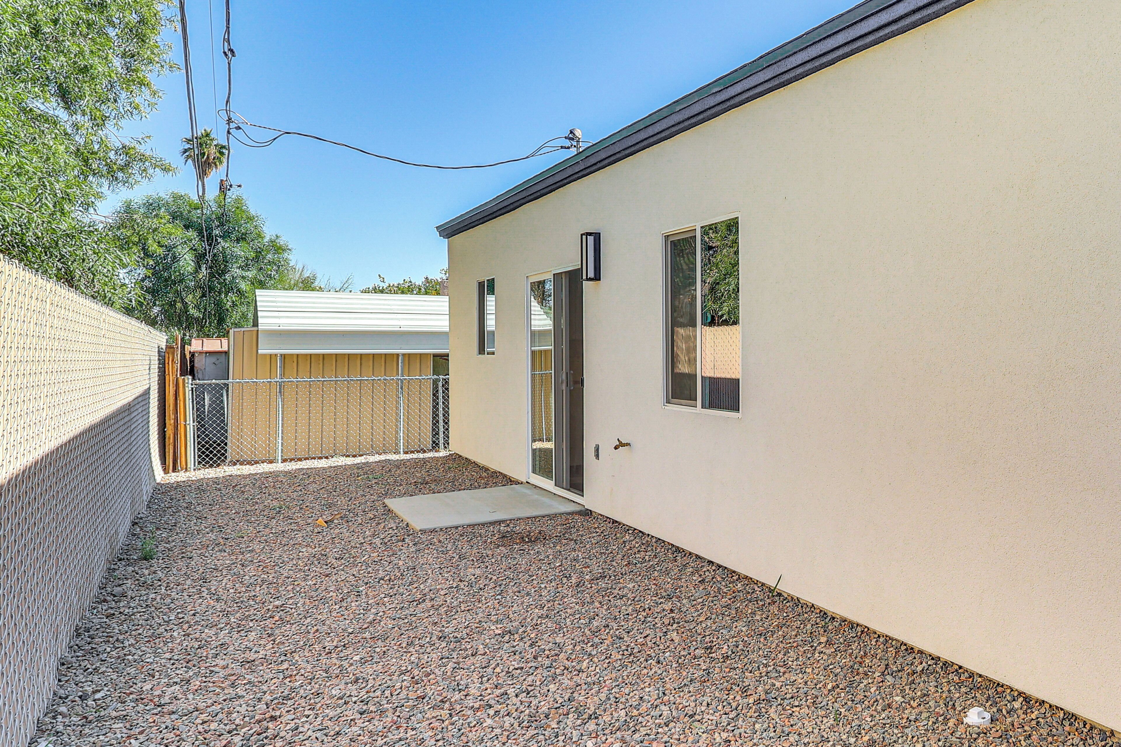 A building with a gravel driveway, a metal fence, and a door leading to a covered area.