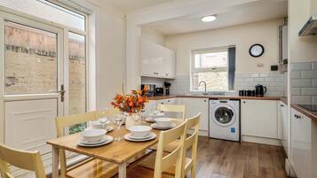A compact kitchen with white cabinets, a washing machine, and a dining area with a table set for four.