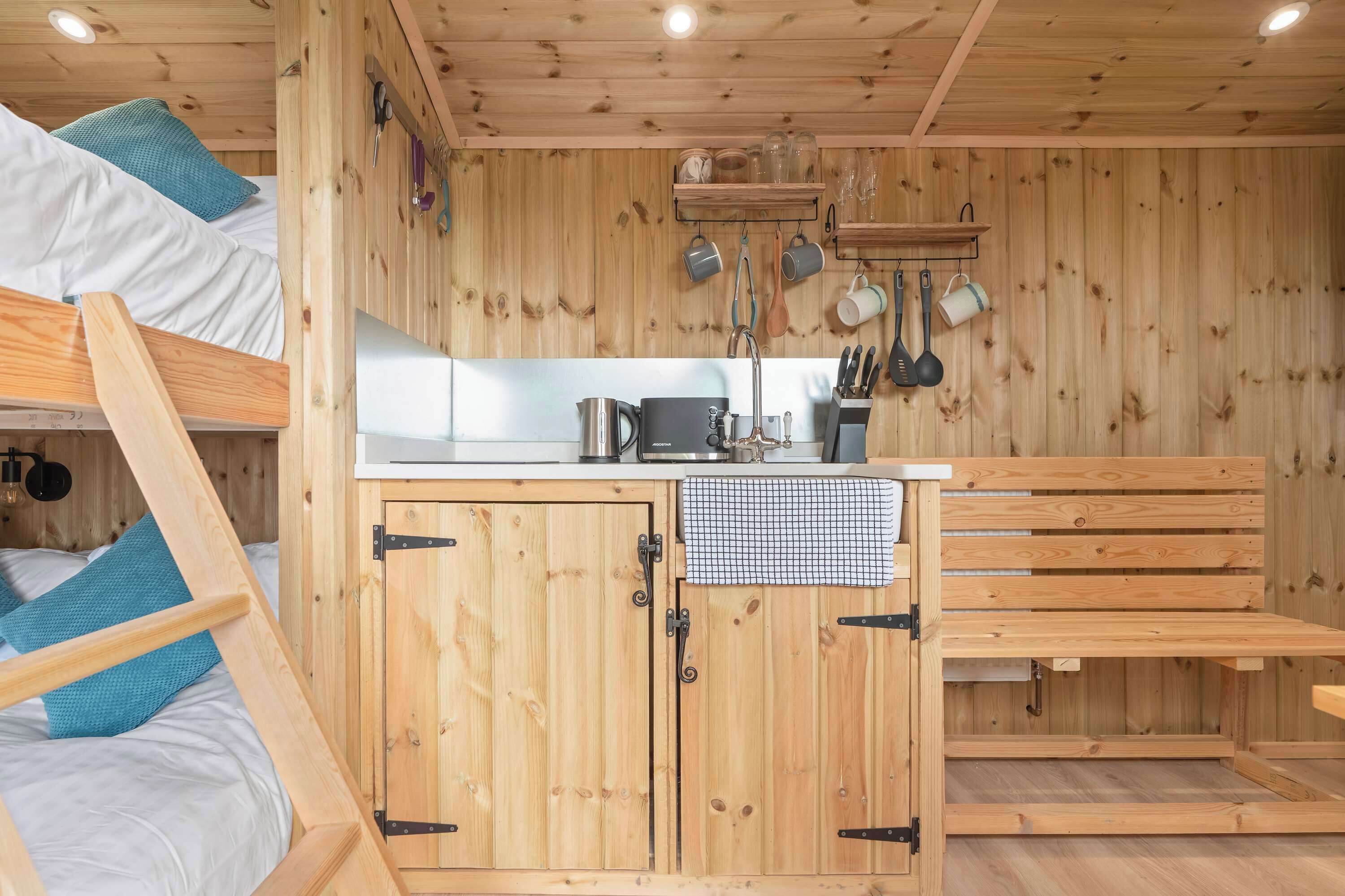 Una habitación pequeña de madera con literas, kitchenette y un banco.