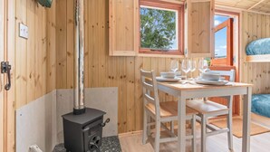 L’intérieur d’un chalet en bois comprend une table à manger pour deux personnes, un poêle à bois et une fenêtre donnant sur la forêt.