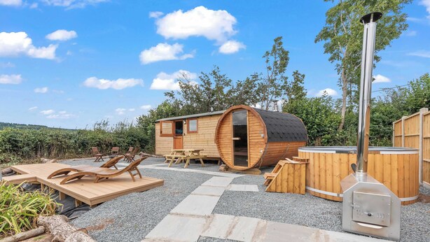 Un chalet rustique en bois, doté d’une grande porte en forme de tonneau, d’un barbecue et d’un espace salon extérieur.