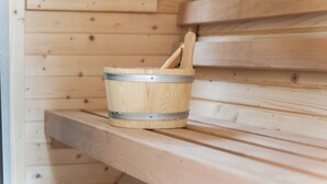 Un banc en bois pour sauna, accompagné d’un seau en métal contenant un maillet en bois.