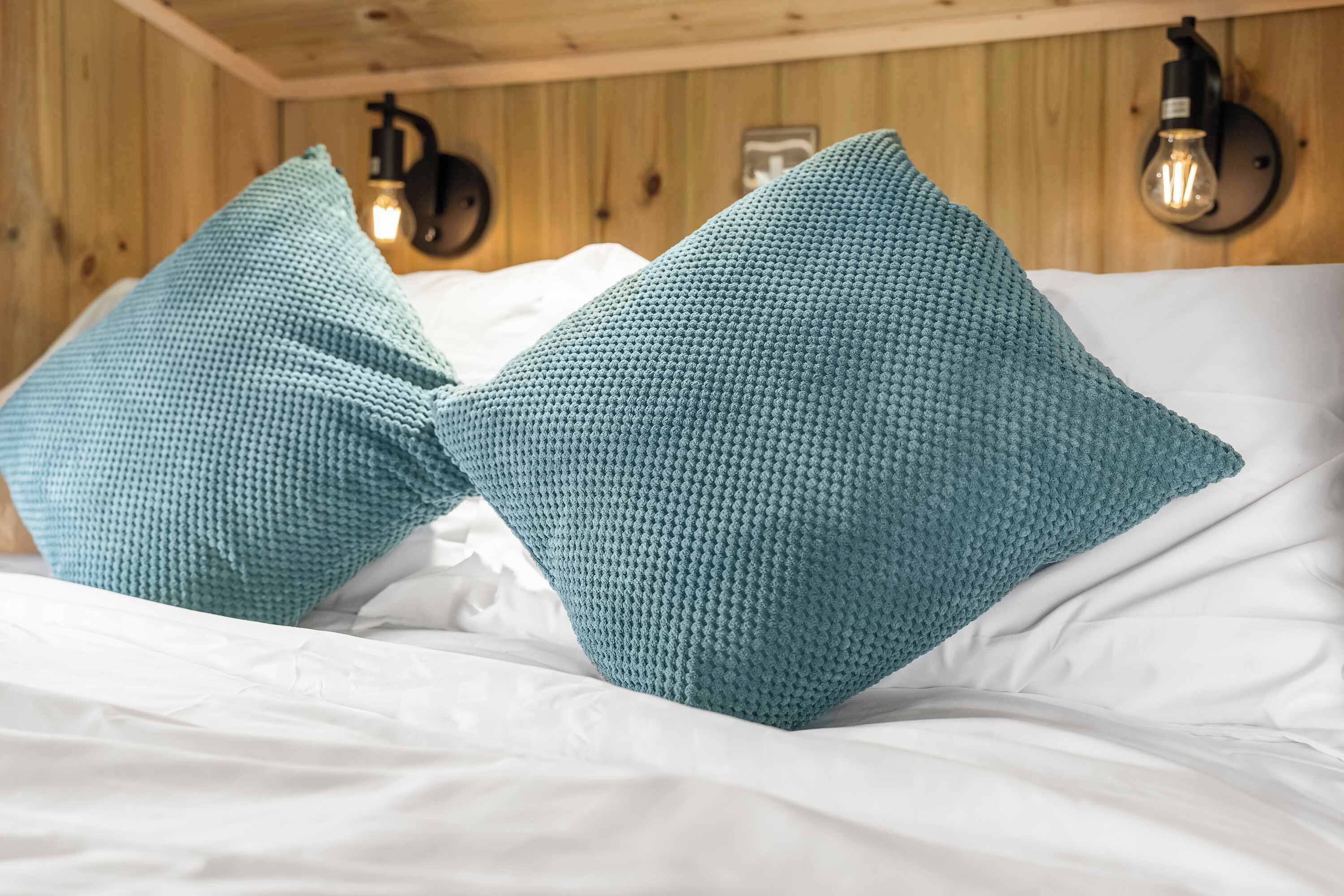 Una cama con sábanas blancas y dos almohadones de punto color turquesa.