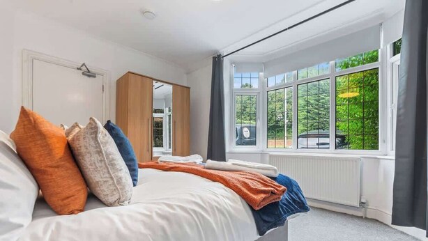 A bedroom with a bed, pillows, a window, and a radiator. - 4-Bed Beeston Getaway | Free Parking (Beeston)