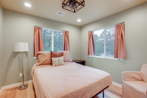 A bedroom with a bed, a chair, a floor lamp, and two windows with curtains. - Cozy Woodland Retreat in the Pines, Near Prescott! (Prescott)