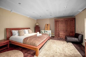 Een slaapkamer met een houten bed, nachtkastje, dressoir, stoel en vloerkleed.