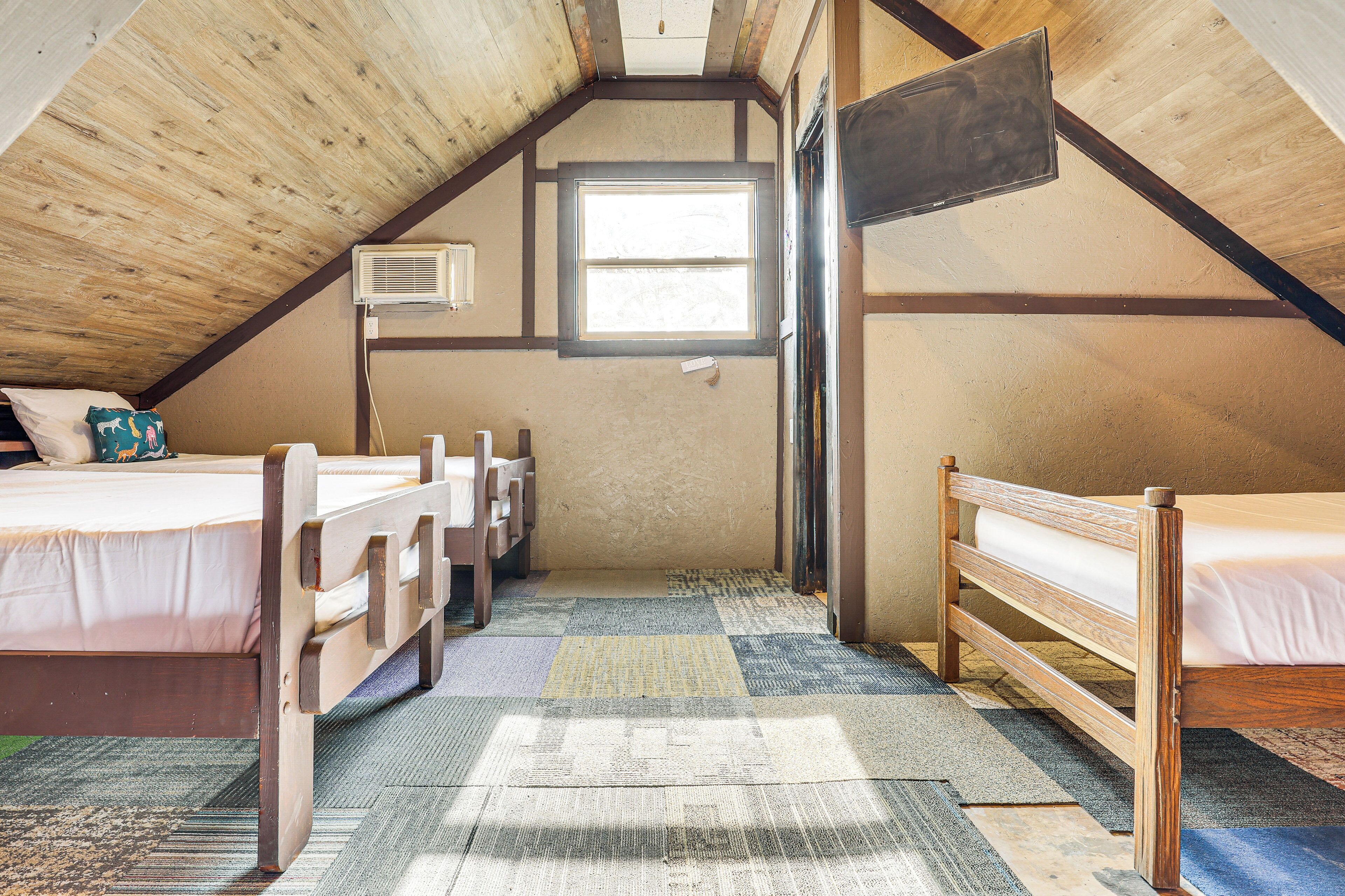 Een kleine, gezellige slaapkamer op zolder met twee houten bedden, een raam en een plafondventilator.