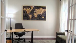 Um espaço de escritório moderno com uma mesa de madeira, cadeira de escritório preta e uma grande pintura abstrata na parede.