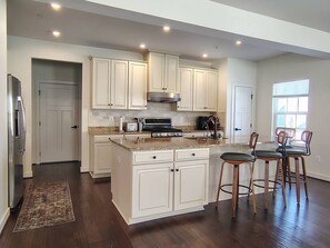 A modern kitchen with white cabinets, a central island, and a dining area with wooden chairs. - Family-Friendly Home in Quiet Neighborhood in Frederick, MD (Frederick)